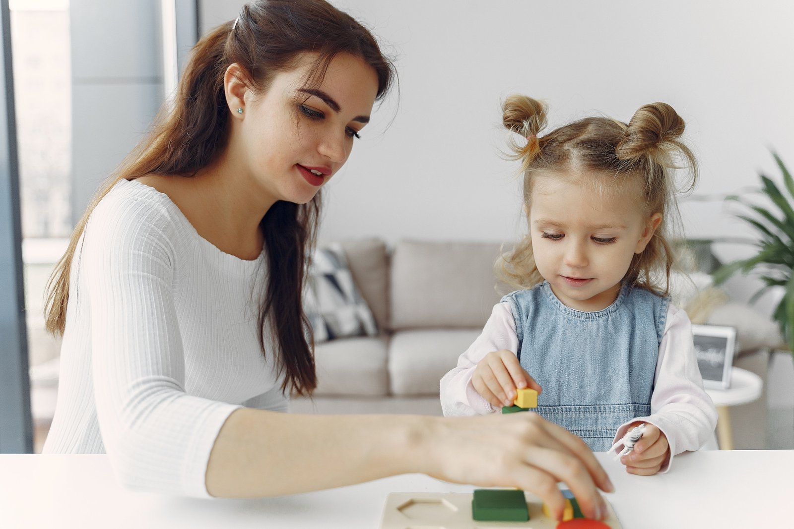 Una sitter gioca con una bambina a un puzzle di forme colorate